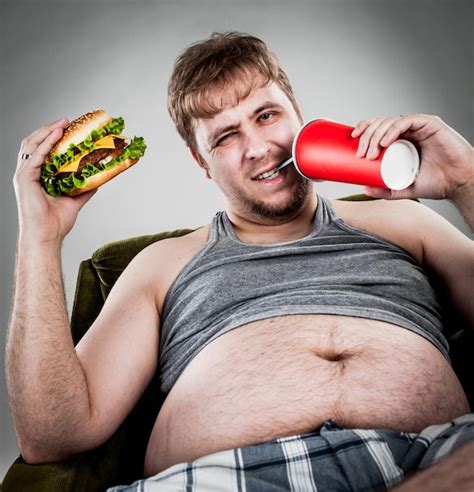 Толстяк ест гамбургер сидя на кресле Премиум Фото