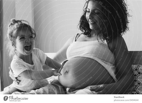 Happy Kid Girl With Her Pregnant Mother On The Bed A Royalty Free