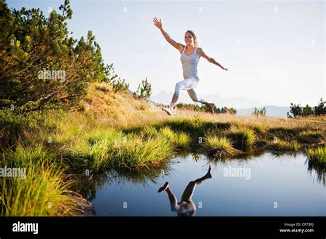 Austria Salzburg County Young Woman Jumping Over Mountain Lake Stock
