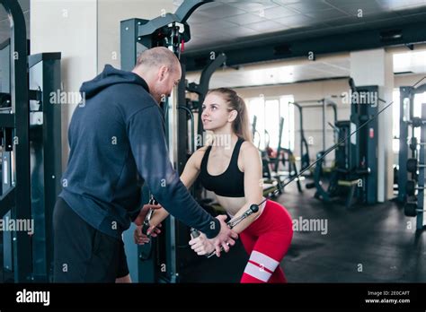 Male Instructor Trains Blonde Woman Doing Exercise In Crossovers In