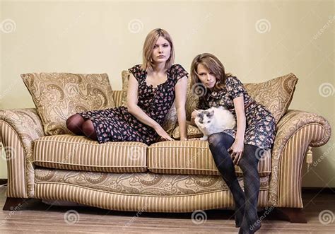 Zwei Schöne Mädchen In Den Kleidern Die Auf Einem Sofa Sitzen