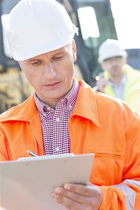 Supervisor Writing On Clipboard At Construction Site With Colleague In