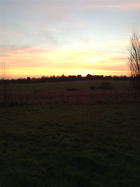 The Sun Is Setting Over An Open Field With A Fence And Trees In The