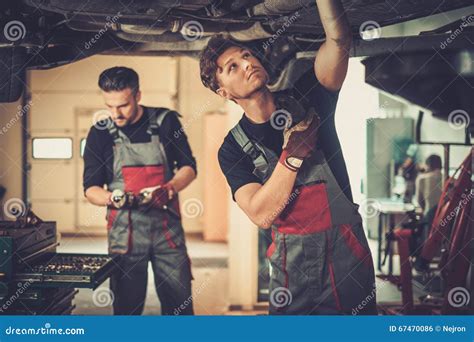 Professional Car Mechanics Working Under Lifted Car In Auto Repair