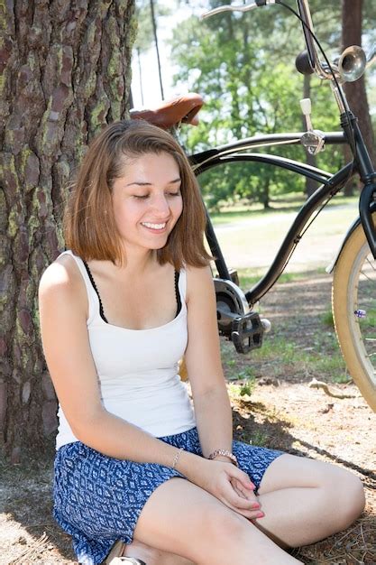 Una hermosa joven está sentada en un árbol con bicicleta negra al aire libre Foto Premium