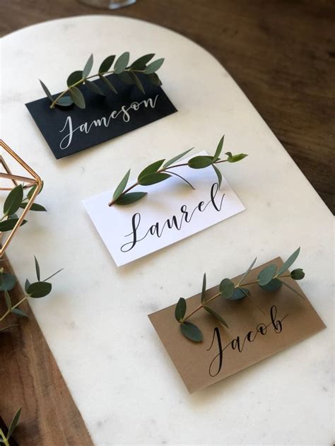 three place cards on a table with greenery and name tags attached to