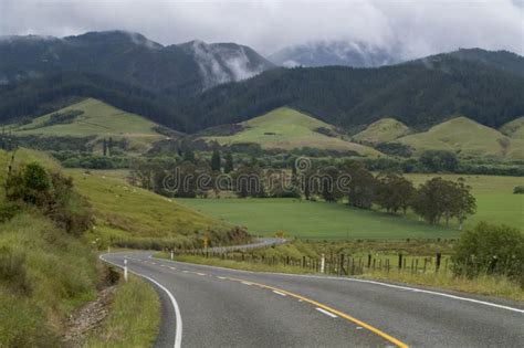 Winding And Scenic Road In New Zealand With Mountains And Green Grass