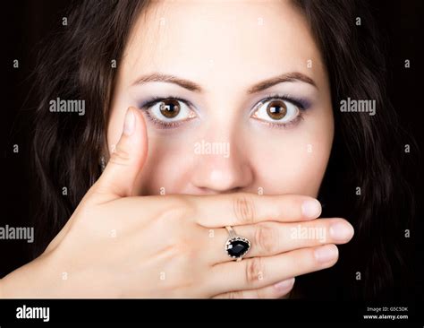 Close Up Woman Looks Straight Into The Camera On A Black Background She Covered Her Mouth With