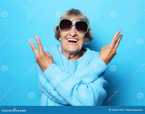 Funny Old Lady Wearing Blue Sweater Hat And Sunglasses Showing Victory