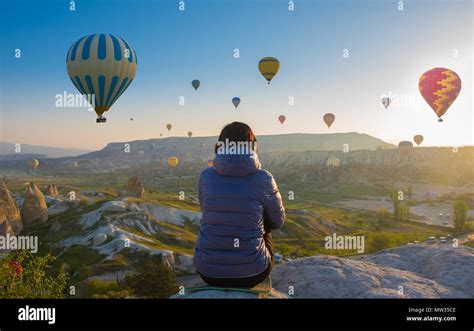 Woman On Top Of Cappadocia Hill In Early Morning Sunrise When Balloons