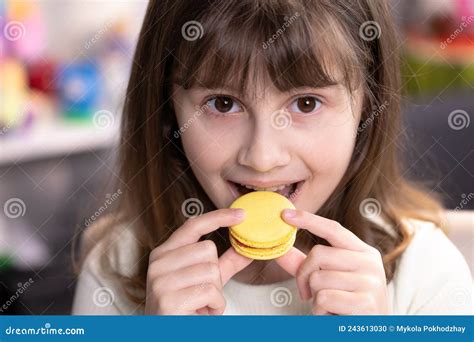 Brunette School Girl On A Home Background Licks Her Lips Eating One Yellow Macaron Dessert