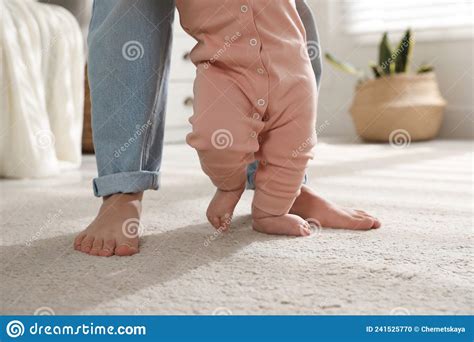 madre apoyando a su hija pequeña mientras aprende a caminar en casa foto de archivo imagen de