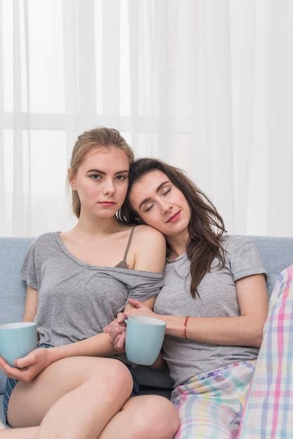 Retrato De Una Pareja De Lesbianas J Venes Sentados En El Sof Sosteniendo Una Taza De Caf Azul
