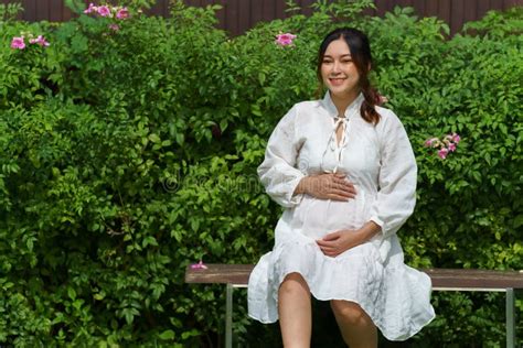 Mujer Embarazada Feliz Sentada En Un Banco En El Parque Foto De Archivo