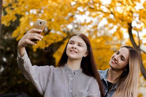 Two Beautiful Smiling Young Girls Taking Selfie On The Phone In The Autumn Park Stock Image