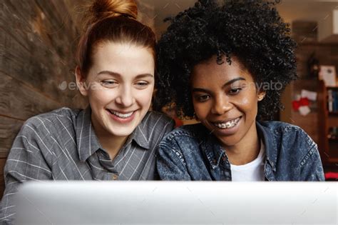 Two Happy Lesbians Sitting In Front Of Open Laptop Computer Together Looking At Screen With