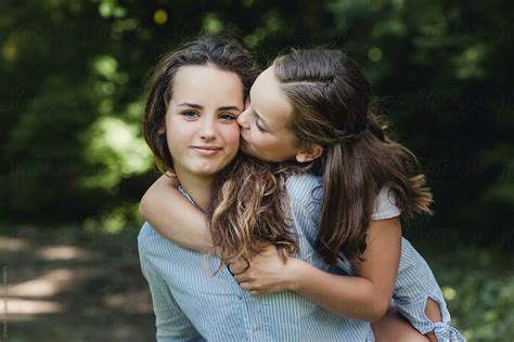 Sweet Portrait Of Little Girl Giving Her Big Sister A Kiss By Stocksy