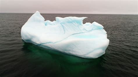 Aerial Rotating Shot Of A Blue Iceberg Floating In Ocean Water Stock