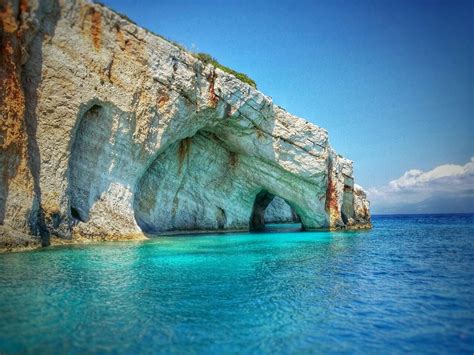 An Ocean Cave With Blue Water And Cliffs In The Background