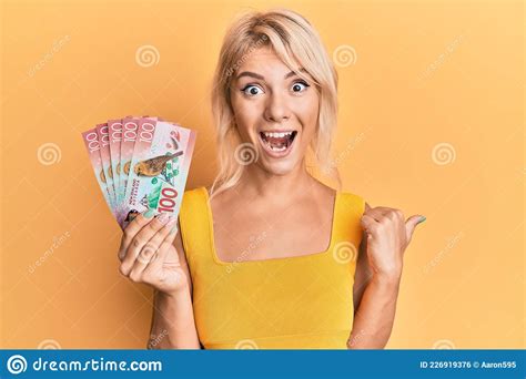 Young Blonde Girl Holding 100 New Zealand Dollars Banknote Pointing