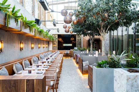 An Indoor Dining Area With Tables Chairs And Potted Plants On The Side