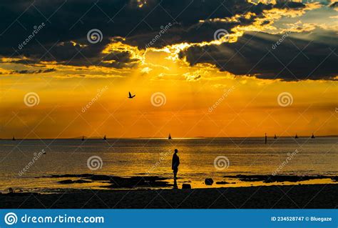 Man Stands On Shoreline Was Sun Begins To Set With Amazing Golden
