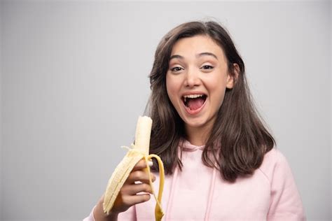 Free Photo Young Woman Eating Banana Over Gray Wall