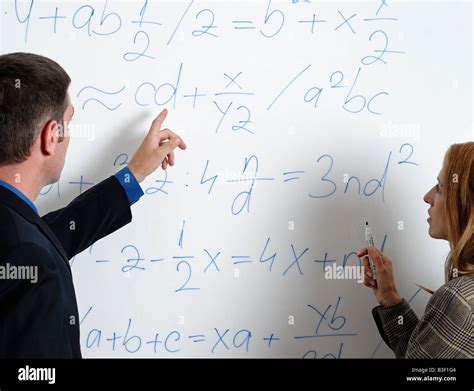 Male And Female Looking At Calculations And Formula On A Whiteboard