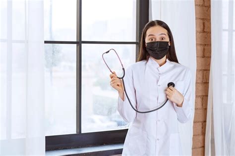 Premium Photo Doctor In Black Mask With A Stethoscope Standing By The Window And Checking The