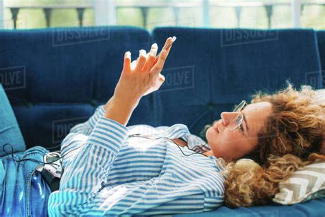 Side View Of Woman Using Smart Phone While Lying On Sofa At Home
