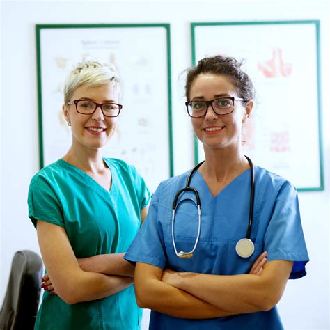 portrait of two professional happy nurses with eyeglasses standing in the office with crossed