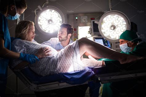 Doctor Examining Pregnant Woman During Delivery While Man Holding Her Hand In Operating Room