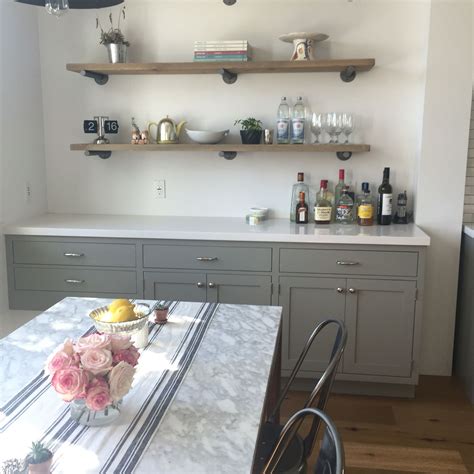 A Kitchen With Gray Cabinets And White Counter Tops Along With Shelves