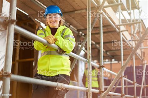 A Female Construction Worker Stands Behind A Scaffold And Smiles To