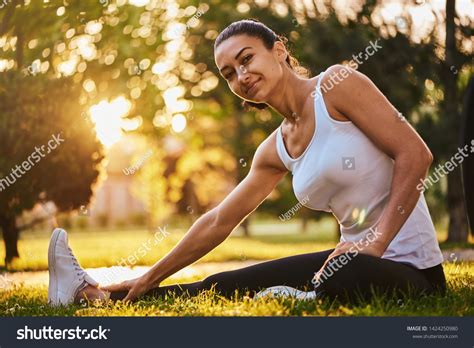 Happy Young Woman Stretching Before Running Outdoors Beautiful Sports Girl In The Park Is