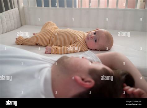 Tired Father Sleeping And His Newborn Son Lying On Bed Looking At