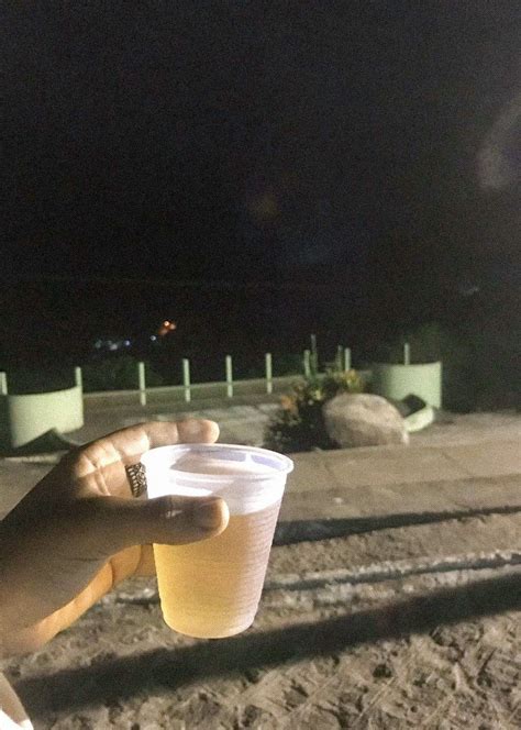 A Person Holding A Cup In Their Hand On The Beach At Night With No One Around