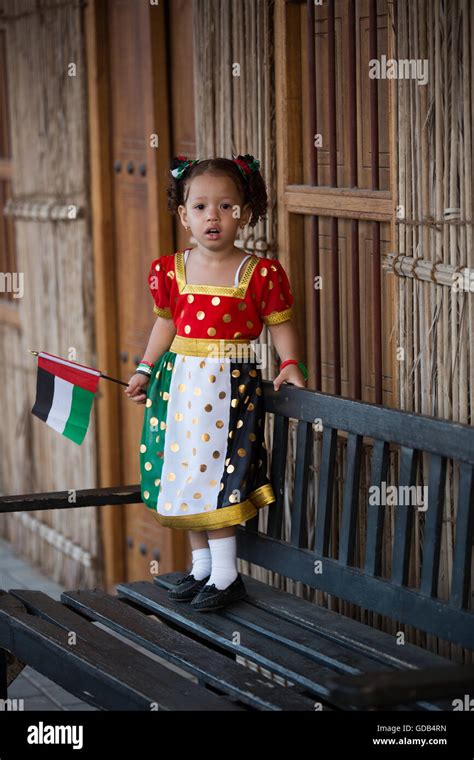 A Young Emirati Girl In A National Day Dress Stands With A Uae Flag On