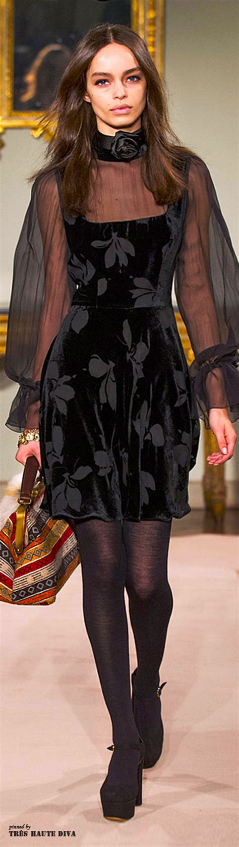 A Woman Walking Down A Runway In A Black Dress