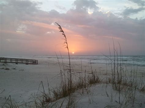 The Sun Is Setting Over The Beach With Sea Oats