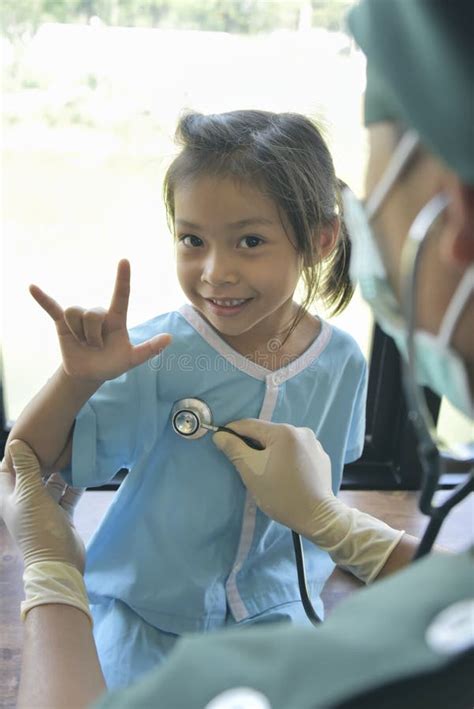 asian doctorin surgical gown examining a little patient girl by stethoscope in office medicine