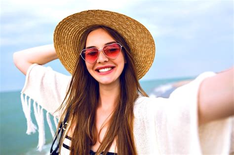 Joven rubia feliz haciendo selfie con sombrero de paja y gafas de sol lindas de corazón