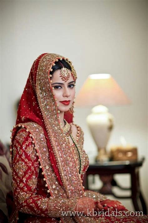 A Woman In A Red And Gold Bridal Outfit Sitting On A Bed Next To A Lamp