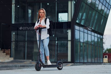 Beautiful Blonde In Casual Clothes Riding Electric Schooter Outdoors At Sunny Daytime Stock