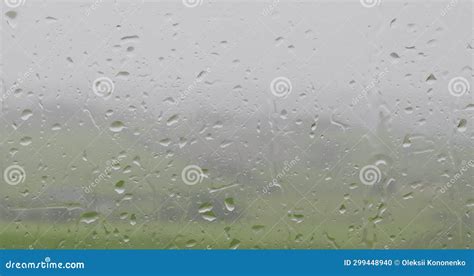 A Raindrops On A Window With A Blurred Green Field In The Background