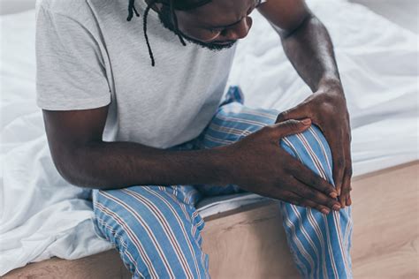 Cropped View Of Young African Man Suffering From Knee Pain In Bedroom