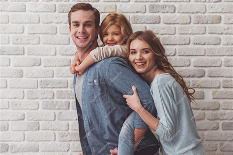 Красивая молодая семья обнимается смотрит в камеру и улыбается стоя у стены из белого кирпича