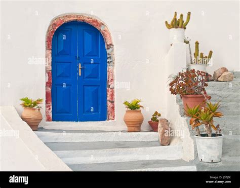 Blue Door Of Beautiful White Greek House With Flower Pots On Stairs In