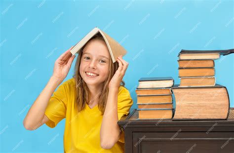 Premium Photo A Girl Holding A Book Above Her Head Next To A Stack Of Books On A Table On A