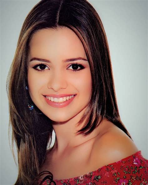 A Woman With Long Brown Hair And Blue Earrings Smiling At The Camera While Wearing A Red Dress